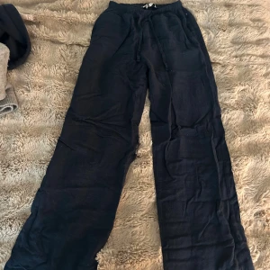 Svarta linnebyxor från Bershka XS - Har hål i sig som kan sys och syns inte när man går. Svarta linnebyxor från Bershka i storlek XS. Byxorna har breda ben, resår i midjan och snörning för extra komfort. Perfekta för chill dagar och har en avslappnad passform. Materialet är svalt linne och färgen är djup svart. 🥰🥰