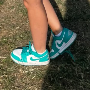 Nike Jordan 1 turkosa sneakers - Snygga Nike Jordan 1 sneakers i turkos och vitt med klassisk swoosh på sidan. Skorna har snörning och en låg siluett som passar perfekt till streetwear. Tillverkade i syntetmaterial och skinn för en cool look.