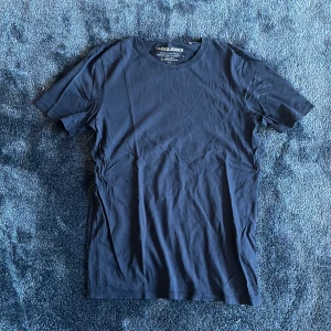 Mörkblå t-shirt från Jack & Jones - Snygg mörkblå t-shirt från Jack & Jones i mjuk ekologisk bomull. Klassisk rund hals och korta ärmar, perfekt för en clean och enkel stil. Passformen är normal och materialet känns skönt mot huden. En basic tee som funkar till allt.