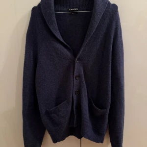 Mörkblå kofta från Tom Ford - Säljer en lyxig mörkblå kofta från Tom Ford med bred krage, knappar framtill och två fickor. Koftan är stickad och har långärmad design, perfekt för lager-på-lager-stil. Tillverkad i Italien och känns riktigt exklusiv.