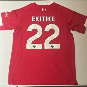 Liverpool Ekiti 22 Adidas matchtröja - Liverpool FC matchtröja från Adidas med Ekiti och nummer 22 på ryggen. Röd bas med vita detaljer, klubbmärke och sponsortryck på bröstet. Tillverkad i lätt och ventilerande Aeroready-material, perfekt för fotbollsplanen eller läktaren. Replika, endast handtvätt gäller!