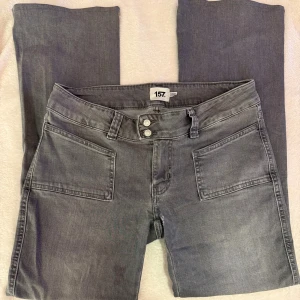 Grå jeansbyxor med bootcut - Grå jeansbyxor från 157 med bootcut och dubbla knappar i midjan. Byxorna har stora framfickor och klassiska bakfickor. Tillverkade i mjukt jeanstyg som ger en avslappnad look. Perfekta för dig som gillar enkel och stilren design. Behöver sys då de gått sönder som syns på bild. Uppsydda så de passar mig (164cm)