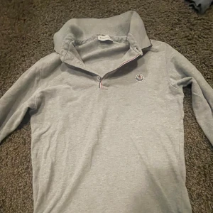 Grå Moncler pikétröja långärmad - Säljer en stilren grå långärmad pikétröja från Moncler. Tröjan har klassisk krage med knappslå och Moncler-logga på bröstet. Materialet är mjukt och skönt, perfekt för dig som gillar en clean look med premiumkänsla.