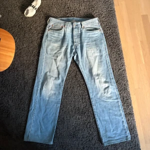 Levi's 501 ljusblå jeans W32 L32 - Klassiska Levi's 501 jeans i ljusblå tvätt. Rak passform med fem fickor och knappgylf. Tillverkade i slitstarkt bomullsjeans, perfekt för en avslappnad och tidlös stil. Levi's Premium-märke på insidan och ikonisk läderpatch bak i midjan.