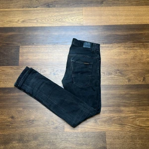 Svarta Nudie Jeans - Säljer dessa fina Nudie Jeans i storlek 33/34! Längd 105 cm, bredd 40 cm. De har en defekt mellan benen som man ser på bilden. Priset är inte hugget i sten. Hör av dig vid frågor! Fraktar oftast samma dag😁