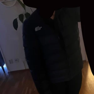 Svart pufferjacka från The North Face XS - Säljer en svart pufferjacka från The North Face i storlek XS. Jackan har en klassisk boxig passform, hög krage och dragkedja framtill. Fylld med dun och har två fickor med dragkedja. Perfekt för kalla dagar och riktigt snygg streetstil. Använt under endast en vinter, pris kan diskuteras vid snabb affär. Inga defekter 