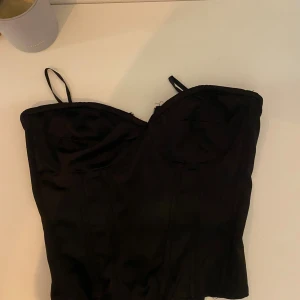 Svart korsett från shein - Säljer en svart korsett med markerade kupor. Toppen har en figurnära passform och är sydd i ett slätt material som ger en snygg siluett. Perfekt för att lyfta vilken outfit som helst.