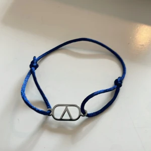 Blått armband med silverdetalj - Snyggt armband med marinblått justerbart band och en stilren silverfärgad detalj i form av en symbol. Perfekt accessoar för att ge din outfit en cool touch.