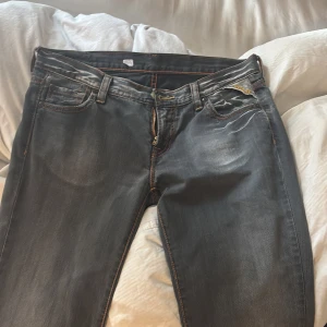 Replay jeans med broderad patch - Mörkblå Replay jeans med slitningar och kontrastsömmar i orange och gul. Broderad patch med blommor baktill och snygga detaljer på bakfickorna. Klassisk femficksmodell i jeansmaterial med dragkedja och Replay-logga vid fickan. Storlek 29, längd 36. Skulle säga att de är lite mindre i storleken och längdmässigt passar någon mellan 170-175 lång. Köpte second hand för 168 kr. Endast provade och väldigt bra skick. 