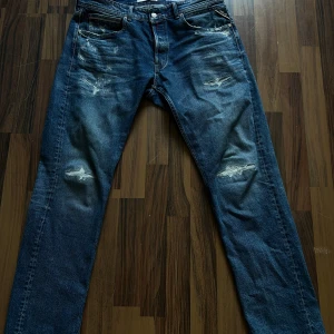 Replay Grover blå slitna jeans - Blå jeans från Replay, modell Grover, med snygga slitningar och distressed detaljer på låren och knäna. Klassisk femficksmodell med läderpatch bak i midjan. Jeansen har rak passform och är tillverkade i robust denim. Storlek är 36 men sitter som 34. Använd fåtal gånger 2000kr nya. 