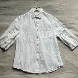 Vit linneskjorta med knappar - Fräsch vit skjorta i linne med klassisk krage och knappstängning hela vägen. Har en bröstficka. Perfekt för en chill och stilren look.