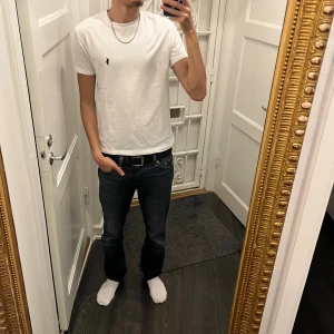 Vit t-shirt från Polo Ralph Lauren - Klassisk vit t-shirt från Polo Ralph Lauren med den ikoniska lilla marinblå polospelaren broderad på bröstet. T-shirten är kortärmad, har rund hals och är tillverkad i mjuk bomull. Perfekt basic-plagg med snygg passform.