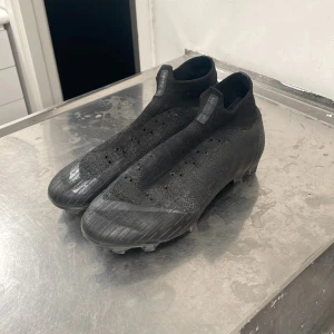 Svarta Nike mercurial fotbollsskor - Säljer ett par svarta fotbollsskor i syntetmaterial. De har en tight passform och är i bra skick, perfekta för fotbollsträning eller match. Skorna har en stilren design med diskreta detaljer och är redo för nya äventyr på planen.