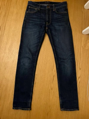 Mörkblå jeans från Nudie Jeans - Säljer ett par mörkblå slim jeans från Nudie Jeans med klassisk orange söm och snygga detaljer på bakfickorna. Modellen har smal passform och är tillverkad i stretchigt bomullsmaterial. Modell Lean Dean och priset är ej hugget i sten🪨🪨