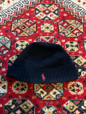 Ralph Lauren mössa - Blå mössa från Ralph Lauren. Mössan är liten. Den har ett litet hål som jag visar på bild, inget som syns direkt