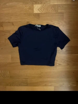 Mörkblå croppad topp från FB Sister - En enkel och stilren mörkblå croppad topp från FB Sister. Modellen har rund halsringning och korta ärmar. Perfekt till jeans eller kjol för en clean look. Materialet känns mjukt och stretchigt.