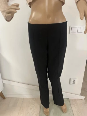 Svarta kostymbyxor med dragkedja - Snygga svarta kostymbyxor med rak passform och diskret dragkedja i sidan. Byxorna har hög midja och är tillverkade i ett slätt tyg som ger en stilren look. Perfekta för dig som gillar klassisk och enkel stil.