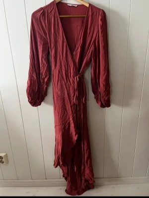 Korallfärgad omlottklänning med volang - Säljer en lång omlottklänning i korall (se sista bilden) med v-ringning och långa puffärmar. Klänningen har knytband i midjan och volangkant nertill. Materialet känns som ett mjukt tyg, troligen polyester eller viskos. Perfekt för dig som gillar en flowy och chic stil.