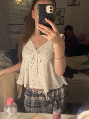 Vit blus med knyt från SHEIN - Supersöt vit blus från SHEIN i storlek XS. Blusen har broderade hålmönster, v-ringning och knyt framtill. Den är ärmlös och har en luftig, lite utställd passform som känns perfekt för varmare dagar.