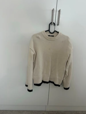 Beige stickad tröja Gina Tricot - Säljer en beige stickad tröja från Gina Tricot i storlek M. Tröjan har svarta detaljer vid ärmslut och nederkant, rund hals och långa ärmar. Perfekt för lager-på-lager och chill dagar. Mjuk och skön känsla med ribbade muddar.