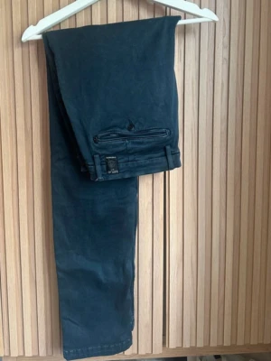 Replay Zeumar svarta byxor, stl 36 - Svarta byxor från Replay, modell Zeumar, med klassisk rak passform och snygga detaljer som knapp och dragkedja vid bakfickan. Materialet är mjukt och har en lätt stretch för extra komfort. Perfekt för dig som gillar stilrena och enkla byxor.