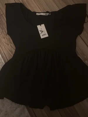 Svart blus med volang från 157 - Säljer en svart blus från 157 i storlek XS. Blusen har korta ärmar och en volang nedtill som ger en snygg och feminin siluett. Perfekt att styla med jeans eller kjol för en trendig look. Materialet känns lätt och bekvämt mot huden.