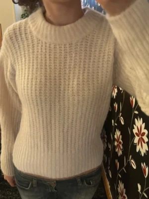 Vit stickad tröja med rund hals - Säljer en vit stickad tröja med rundad hals och långärmade ärmar. Tröjan har ett grovt ribbat mönster och sitter snyggt med en normal passform. Perfekt att matcha med jeans eller kjol för en chill look.