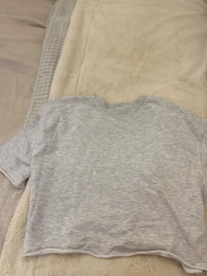  Ljusgrå kortärmad sweatshirt💕 - Stilren ljusgrå kortärmad sweatshirt/topp i mjukt och bekvämt material. Avslappnad passform med rund halsringning och lätt rå/rolled kant nertill som ger en modern och minimalistisk look. Perfekt att styla med jeans, kjol eller över en klänning för en trendig lager-på-lager-outfit. Funkar lika bra till vardags som till lounge/mys.  Plagget är i fint skick och väl omhändertaget endast använd 1 gång.  ✨ Detaljer: – Färg: Ljusgrå – Passform: Avslappnad – Hals: Rund – Ärmar: Kortärmade