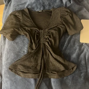 Svart topp med puffärm från BikBok - Säljer en svart topp från BikBok i storlek XS. Toppen har puffärmar, v-ringning och snygg snörning framtill som ger en rynkad effekt. Mycket bra skick, perfekta till vardag, sommar eller fest! 