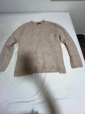 Beige stickad tröja från BikBok - Mysig beige stickad tröja från BikBok i storlek XS. Tröjan har rund hals, ribbade muddar och långärmad passform. Perfekt för kyliga dagar och enkel att matcha med jeans eller kjol. Materialet är mjukt och ger en skön känsla.