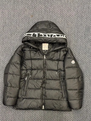 Svart Moncler pufferjacka med huva - Svart Moncler herrjacka i nytt skick. Klassisk och stilren modell som passar perfekt för vinter och kallare dagar. Jackan är varm, lätt och håller mycket hög kvalitet. Endast provad, inga defekter. Skickas snabbt 💨