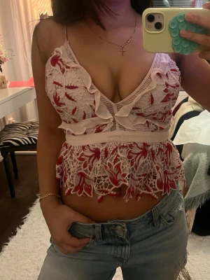 Rosa och röd spetsig blommig linnetopp - Säljer en superfin linnetopp med tunna axelband och blommigt spetsmönster i rosa och rött. Toppen har volangdetaljer, v-ringning och en snygg dragkedja i ryggen. 