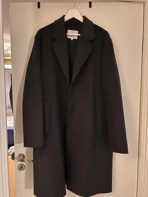 Bläck Men’s Black Wool Overcoat – Scandinavian Tailoring – Size 54 (L) - Timeless men’s black long coat from bläck – Scandinavian Tailoring. Clean, minimalist design with a classic tailored fit. Perfect for both formal and smart-casual outfits.  High-quality fabric with a structured feel. Works great over a suit or styled casually with knitwear and boots  Details: 		Brand: bläck 		Color: Black 		Size: 54 (EU) – fits Large (L) 	Style: Long coat / overcoat 		Fit: Classic / tailored 		Condition: Very good 		Season: Autumn / Winter 		Original retail price: 2500kr/220 eur