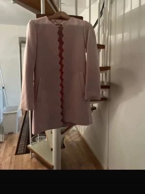 Blush Pink Elegant Coat with Scalloped Edge – Size EU 34 / US 4 - Beautiful blush pink coat in a clean, elegant design. Features a unique scalloped (wave) edge along the front opening and a decorative gold-tone chain inside the neckline. Soft structured fabric Long sleeves Two front pockets Feminine and timeless style Perfect for spring, autumn, occasions, or everyday chic looks Gently used and in very good condition. Size: EU 34 / US 4 / CA 4 / MX 4 (Please check measurements if needed.) Feel free to message me if you have any questions 🌸 