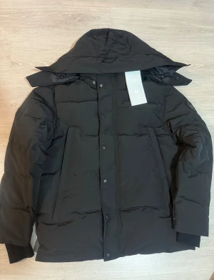  Canada Goose - Svart Canada Goose jacka (wyndham)med svart logo i storlek M.  Jackan är quiltad, har knappar framtill och är tillverkad i slitstarkt material. Perfekt för kalla vinterdagar och har en clean, stilren look. Kan ge bra pris vid snabb affär, skicka dm om du undrar något eller vill ha mer bilder. Pälsen och påsen följer med.👍.