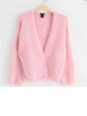 Rosa stickad kofta från Vero Moda - Mysig ljusrosa stickad kofta från Vero Moda med djup v-ringning och långärmad design. Koftan har en loose passform och är tillverkad i ett fluffigt material som känns extra skönt under kyliga dagar. Perfekt att slänga över en t-shirt eller linne.