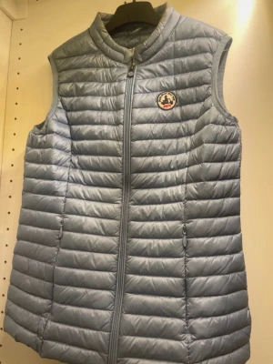 Ljusgrå dunväst från JOTT - Säljer en ljusgrå dunväst från JOTT med quiltad design och rund krage. Västen har dragkedja framtill och två sidofickor med dragkedja. Märkets logga är broderad på bröstet. Står ingen storlek men skulle säga xxs-xs Obs lite smink fläckar längst upp vid kragen se bild!