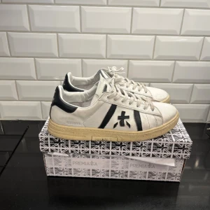 Premiata vita sneakers med svarta detaljer - Säljer dessa feta premiata skor. Storlek 44/45 passar även folk med 45 dådå. Skicket är 8/10 lite använda med ingenting som ej går bort med lite rengöring. Nypris är väl runt 2300kr correct me if I’m wrong… 