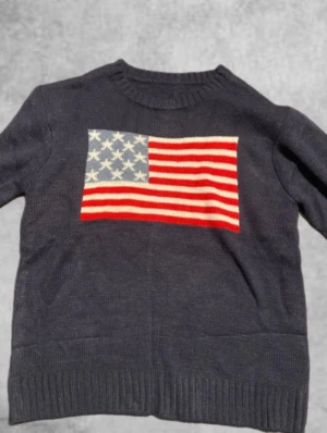 Mörkblå stickad tröja med USA-flagga - Snygg mörkblå stickad tröja med en stor amerikansk flagga på bröstet. Lite pösig vid armarna, passar 150-164