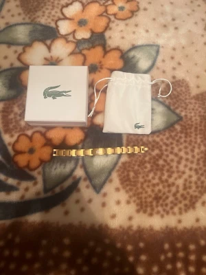 Guldfärgat armband från Lacoste - Lacoste armband med original box har gjort den till 18 cm men kan fixa den till 22cm igen om det behövs eller de du önskar. 