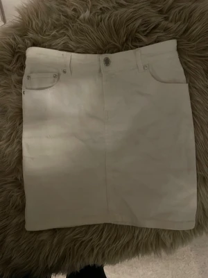 Vit jeanskjol med fickor - Snygg vit jeanskjol från Amisu med klassisk femficksdesign, bälteshällor och dragkedja framtill. Kjolen är rak och kort (lite längre än halvvägs ner till knäna), perfekt till sneakers eller boots. Materialet är kraftig bomull som ger en stabil känsla.