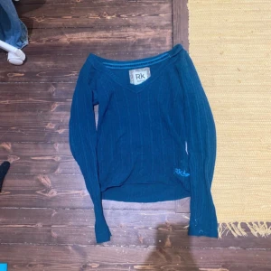 Blå ribbad tröja från RK - Mysig blå långärmad tröja från RK med v-ringad hals och ribbad struktur. Perfekt för lager på lager under kyliga dagar. Enkel och stilren design som passar till det mesta.