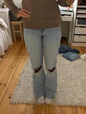 Ljusa ripped jeans från Zara - Säljer ett par ljusblå jeans från Zara. Jeansen har stora slitningar vid knäna och mindre slitningar på låren, klassisk femficksdesign och dragkedja med knapp. Perfekt för dig som gillar en chill och edgy stil. Innerbenslängd : 87 Midjemått: 34