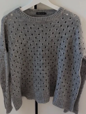 Grå stickad prickig tröja Made in Italy - Säljer en grå stickad tröja med prickigt hålmönster från Made in Italy. Tröjan har rund hals, ribbade muddar och lång ärm. Perfekt för dig som gillar en chill och snygg look med lite extra detaljer.