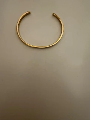 Jack bangle från Edblad - Säljer en guldig bangle från Edblad i modellen Jack (unisex). Armbandet har en brede på 4 mm och eb höjd på 2,5 mm. Den är i blank 14k guldplätering på rostfritt material. Den är nickelsäkert och vattentålig. Den är endast prövad!. Justerbar