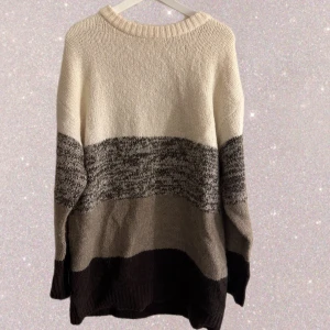 Randig stickad tröja i neutrala toner - Säljer en mysig stickad tröja med breda ränder i beige, grått och svart. Tröjan har rund hals och långärmad passform, perfekt för kyliga dagar. Materialet är mjukt och ger en avslappnad, loose känsla. Enkel att matcha med jeans eller leggings.