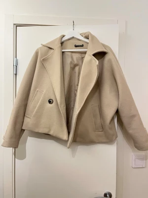 Beige kappa  - Snygg beige kappa med klassisk krage och en knapp framtill. Jackan är croppad och lite oversized , jag är en xs så skulle säga att jackan är en S/M, de finns två fickor på varje sida och är Fodrad insida för extra komfort. Jackan är i gott skick de enda är att de är ett hål inuti ena fickan