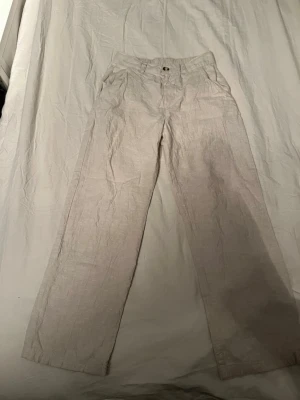 Beige linnebyxor från Kappahl, strl 152 - Snygga beige linnebyxor från Kappahl i storlek 152. Byxorna har rak passform, elastisk midja och knapp framtill. Perfekta för varma dagar och har en stilren look med klassisk design. Materialet är linne som ger en skön och luftig känsla.
