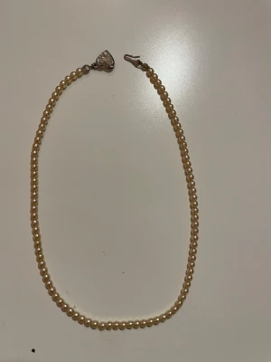 Snyggt pärlhalsband med hjärtformat lås - Pärlhalsband med champagnefärgade pärlor och hjärtformat lås med små diamanter på.