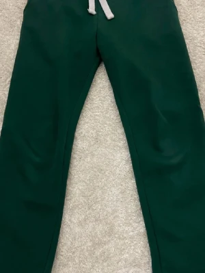 Mörkgröna mjukisbyxor från russemerch  - Mörkgröna mjukisbyxor i storlek S med bred resår i midjan och vit snörning framtill. De har lite nötningar i skrevet, se bild 4, men de märks inte när man har de på sig☺️ de är också lätt att fixa ifall man vill till exempel att sy in lite grann🥰🥰